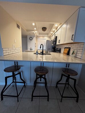 Une cuisine moderne avec des armoires blanches, un robinet noir et trois tabourets en bois.