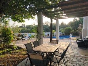 Un patio al aire libre con mesa y sillas, una piscina y abundante vegetación.