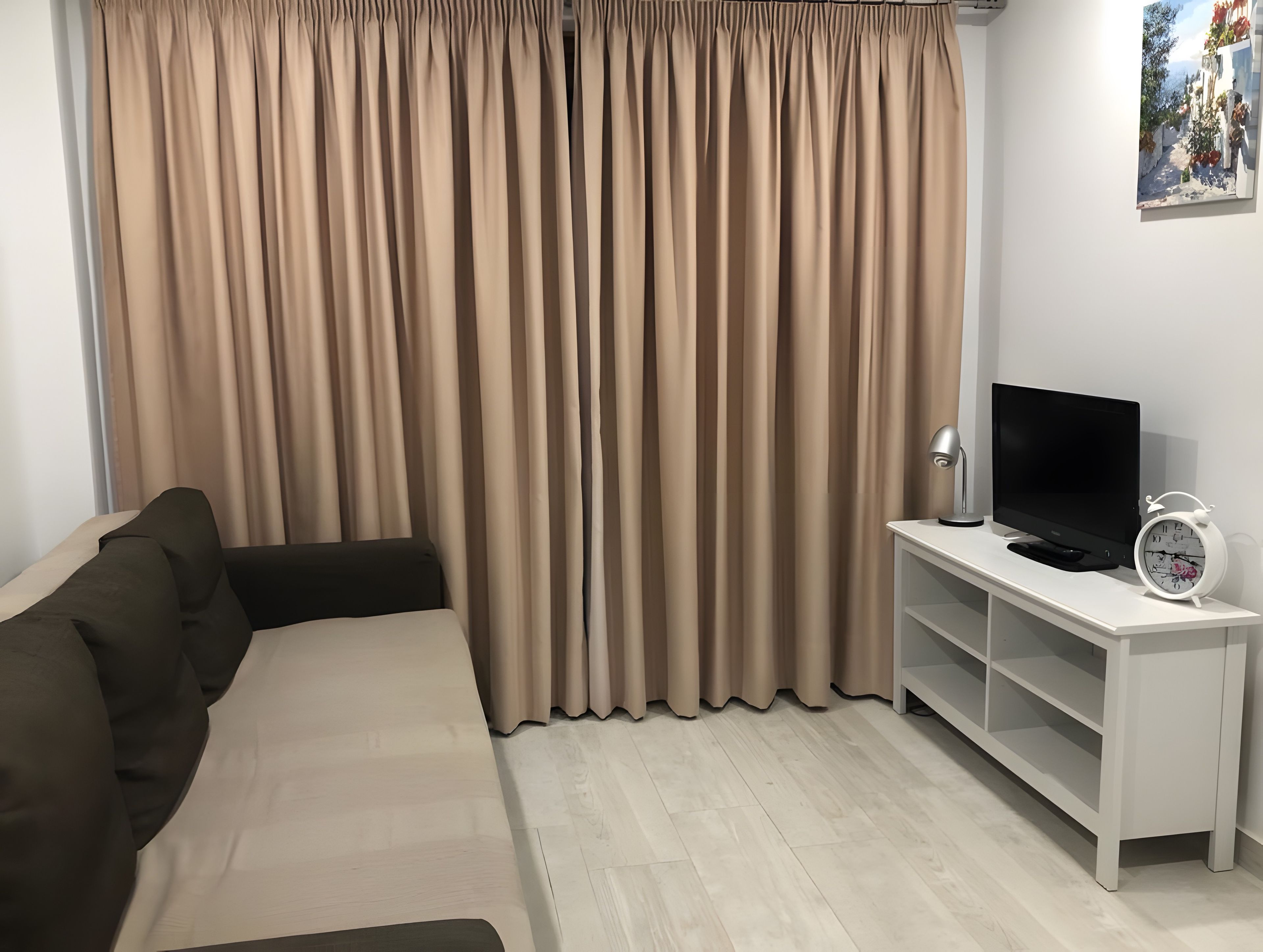 A living room with a sofa, a TV on a stand, a clock, and curtains.