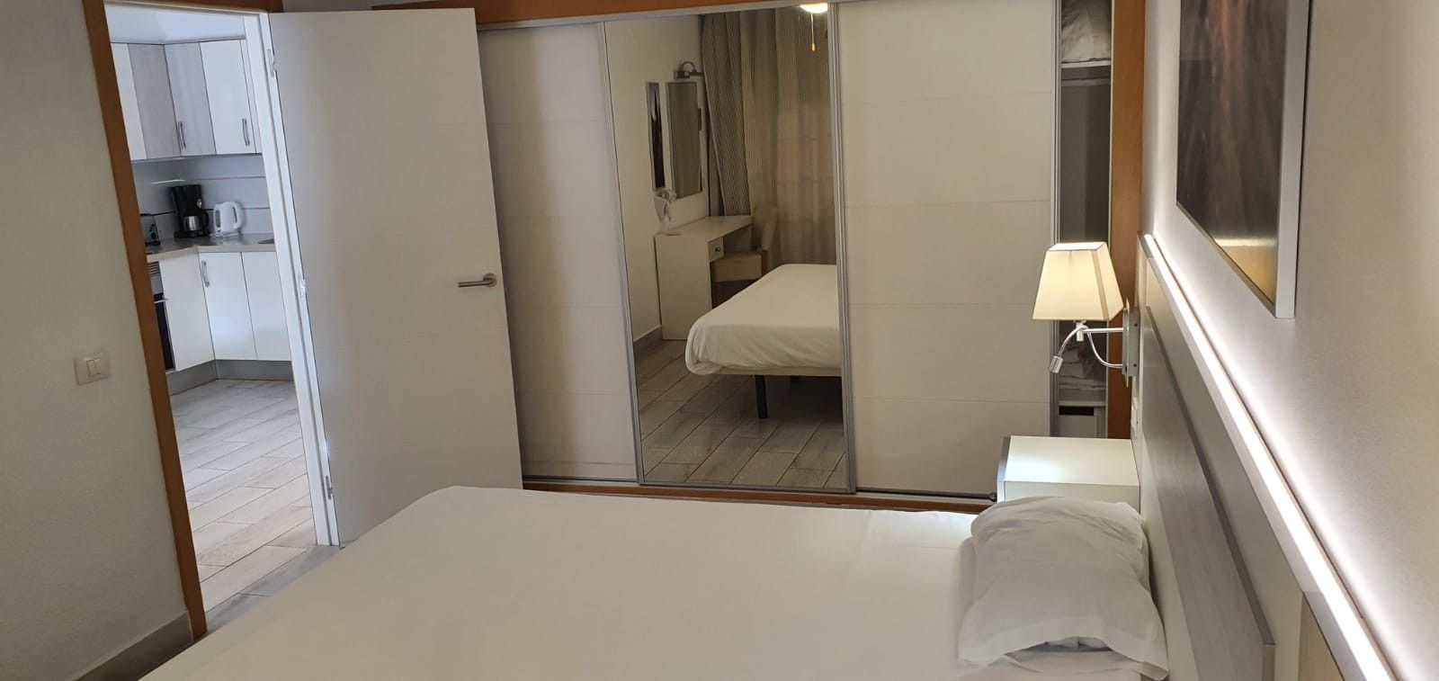 Een hotelkamer met een bed, nachtkastje, lamp, spiegel en uitzicht op de badkamer.