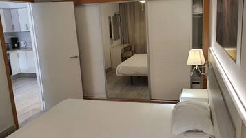 Een hotelkamer met een bed, nachtkastje, lamp, spiegel en uitzicht op de badkamer.