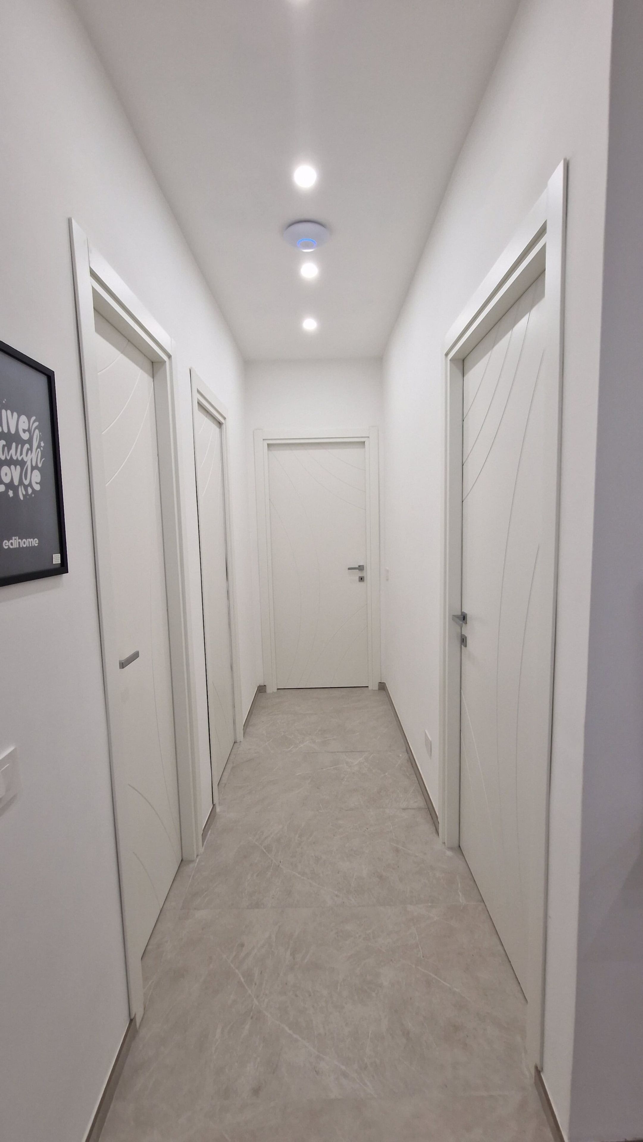 A hallway with white walls, a tiled floor, and doors on both sides leading to rooms.