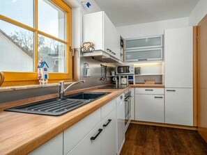 A compact kitchen with white cabinets, a wooden countertop, a sink, a microwave, and a stove. - 6/t5 Holiday Home Park \"freesenbruch\" (Zingst)