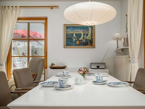 A dining area with a table set for tea, a painting of a seascape, and a window with curtains. - 6/t5 Holiday Home Park \"freesenbruch\" (Zingst)