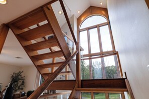 A wooden staircase leading to a loft area with a large arched window providing a view of the outdoors.