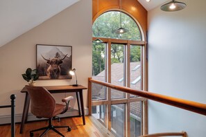 A modern room with a desk, chair, and a large window with a view of trees.