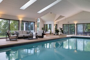 A modern indoor swimming pool area with a pool, seating, and large windows.