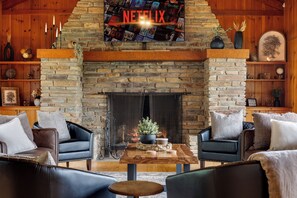 A cozy living room with a stone fireplace, leather sofas, and a Netflix sign above.