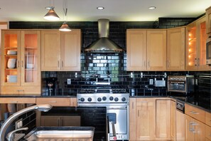 A kitchen with wooden cabinets, a black tiled backsplash, stainless steel appliances, and pendant lighting.
