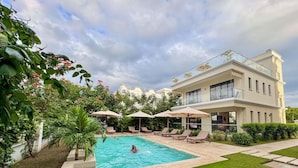 Ein modernes, zweistöckiges Gebäude mit Swimmingpool, Liegestühlen und Sonnenschirmen.