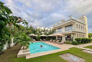 Ein modernes, zweistöckiges Gebäude mit Swimmingpool, Liegestühlen und Sonnenschirmen.