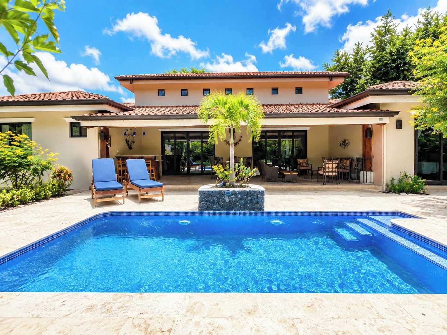 A swimming pool with lounge chairs, a patio area, and a building with a tiled roof.