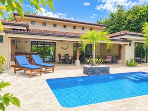 Ein Poolbereich mit Schwimmbecken, Liegestühlen und einer überdachten Terrasse mit Gartenmöbeln.