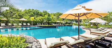 A swimming pool with lounge chairs and umbrellas, surrounded by greenery.