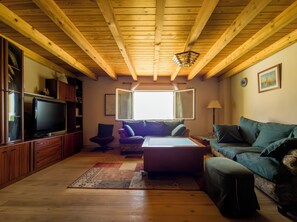 A living room with a wooden ceiling, a television, a sofa, and a window.