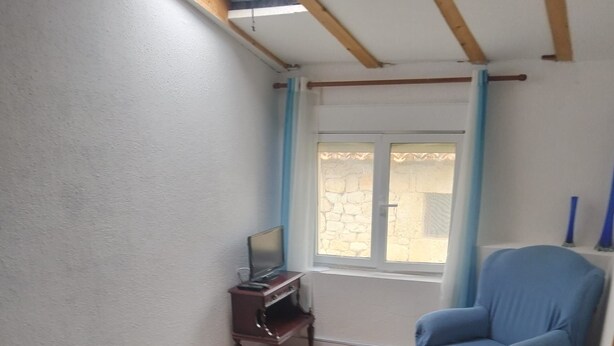 Une pièce comprenant un lit, une chaise, une petite table avec un téléviseur et une fenêtre avec des rideaux.