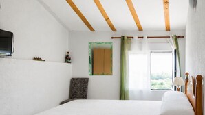 Une chambre avec un grand lit, des poutres en bois au plafond, un téléviseur fixé au mur et une fenêtre avec des rideaux.