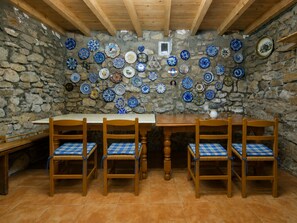 A stone-walled dining area with a wooden table and chairs, and a variety of decorative plates on the wall.
