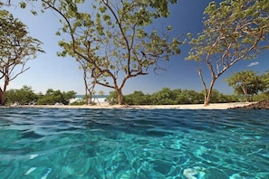 A clear view of a swimming pool with trees and a sandy beach in the background. - 3-Bedroom Villa in Hacienda Pinilla (Pinilla)