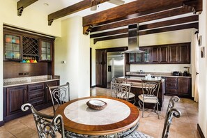 A spacious kitchen with dark wooden cabinets, a central island, and a round dining table with chairs. - 3-Bedroom Villa in Hacienda Pinilla (Pinilla)