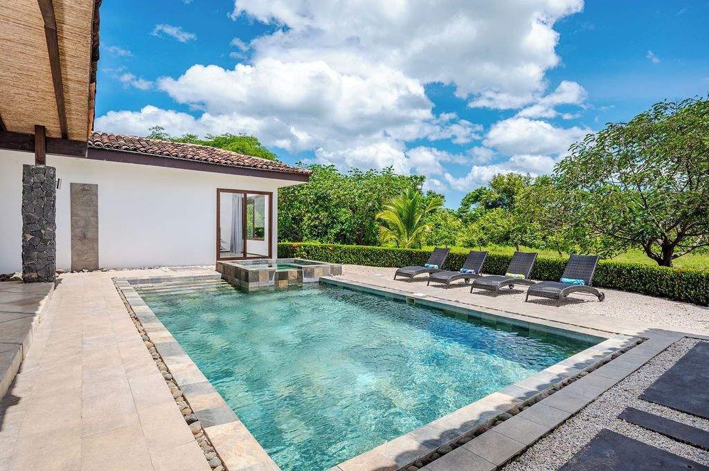 Piscina com espreguiçadeiras, muro de pedra e céu azul límpido.