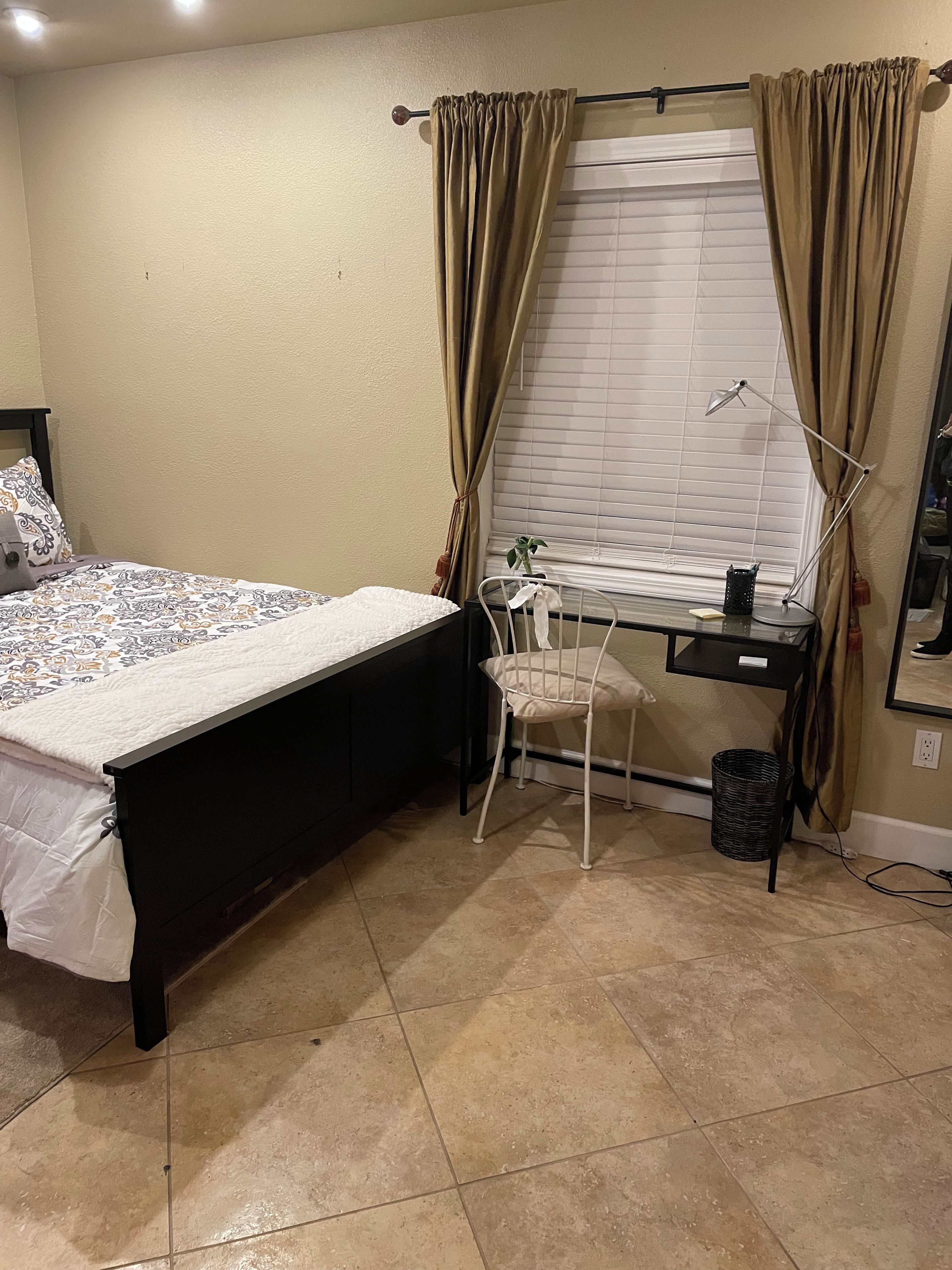 Un dormitorio con cama, escritorio, silla, ventana con persianas y lámpara.