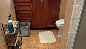 Ein Badezimmer mit einem Holzbadezimmerhocker, einer Toilette, einer Duschkabine und einem gefliesten Boden.