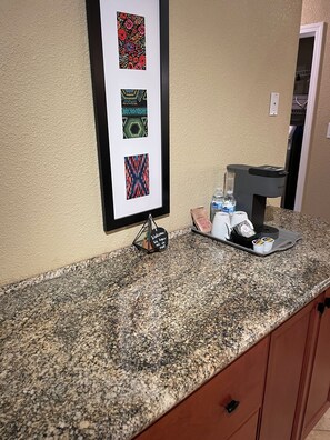 A kitchen counter with a coffee maker, a tray with cups and a bag of snacks, and a framed artwork above. - Private, Stylish Studio w/ Separate Entrance—Spacious, Serene & Comfortable (Oakland)