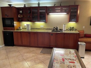 A kitchen with wooden cabinets, a built-in microwave, a sink, and a countertop with various items. - Private, Stylish Studio w/ Separate Entrance—Spacious, Serene & Comfortable (Oakland)