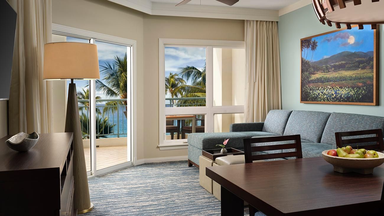 Una camera d'hotel con balcone, un divano, un tavolo da pranzo e un quadro.