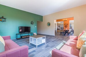 Ein Wohnzimmer mit Fernseher, Sofas und einem Couchtisch. Es gibt eine Essecke mit Stühlen und einem Tisch.