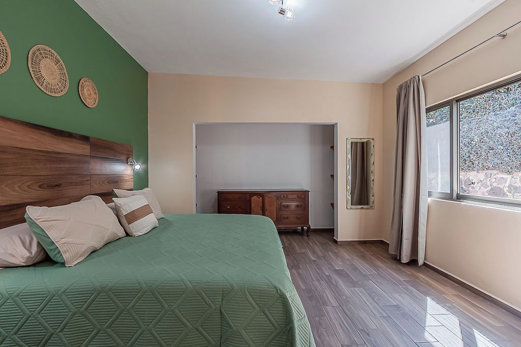 A bedroom with a bed, dresser, and a window with curtains.