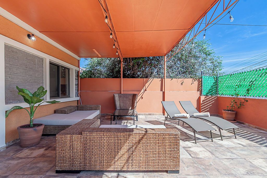 An outdoor patio with a covered seating area, a lounge chair, and a potted plant.