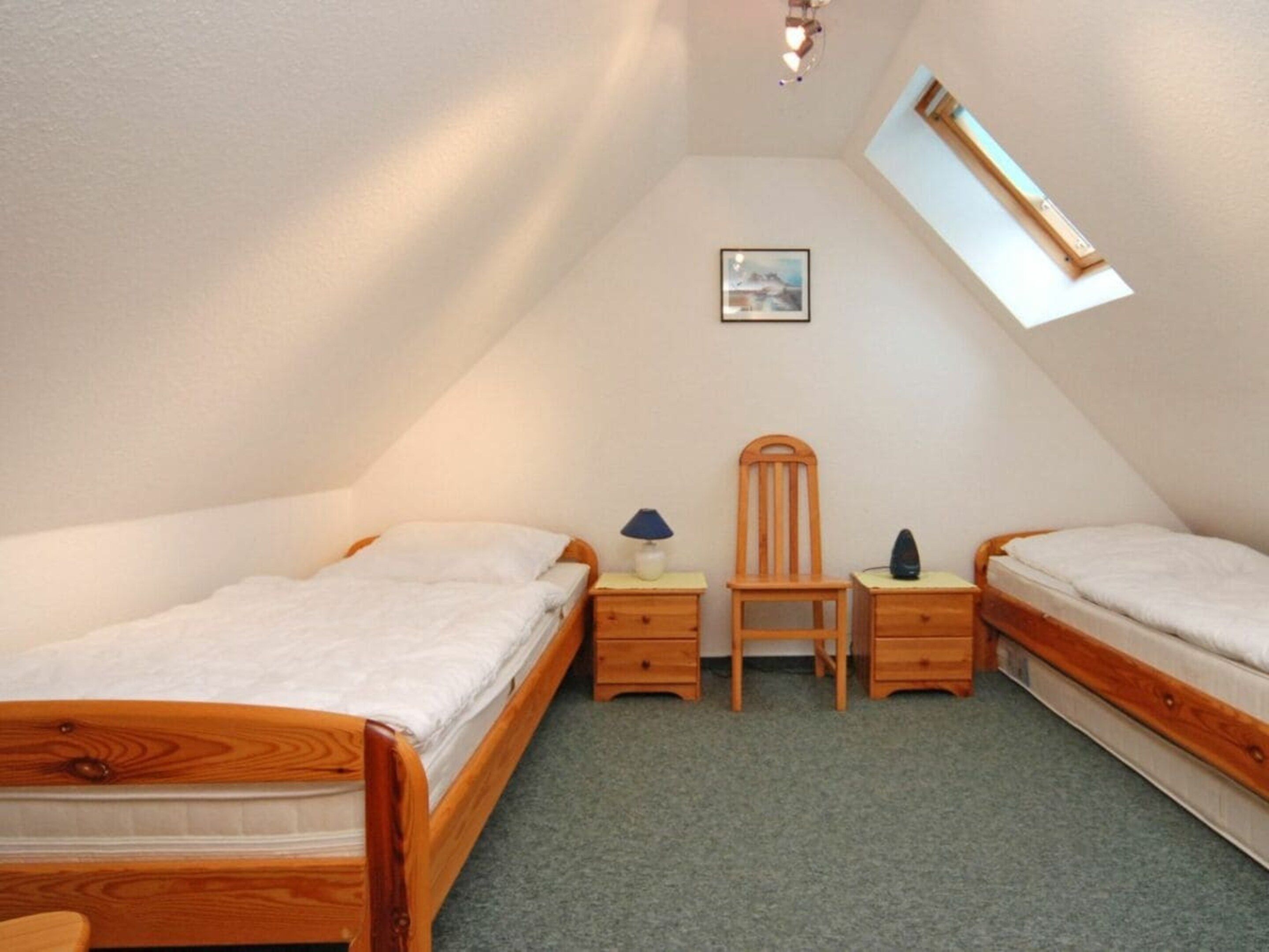 A small, triangular attic bedroom with two wooden beds, a desk, a chair, and a small window.