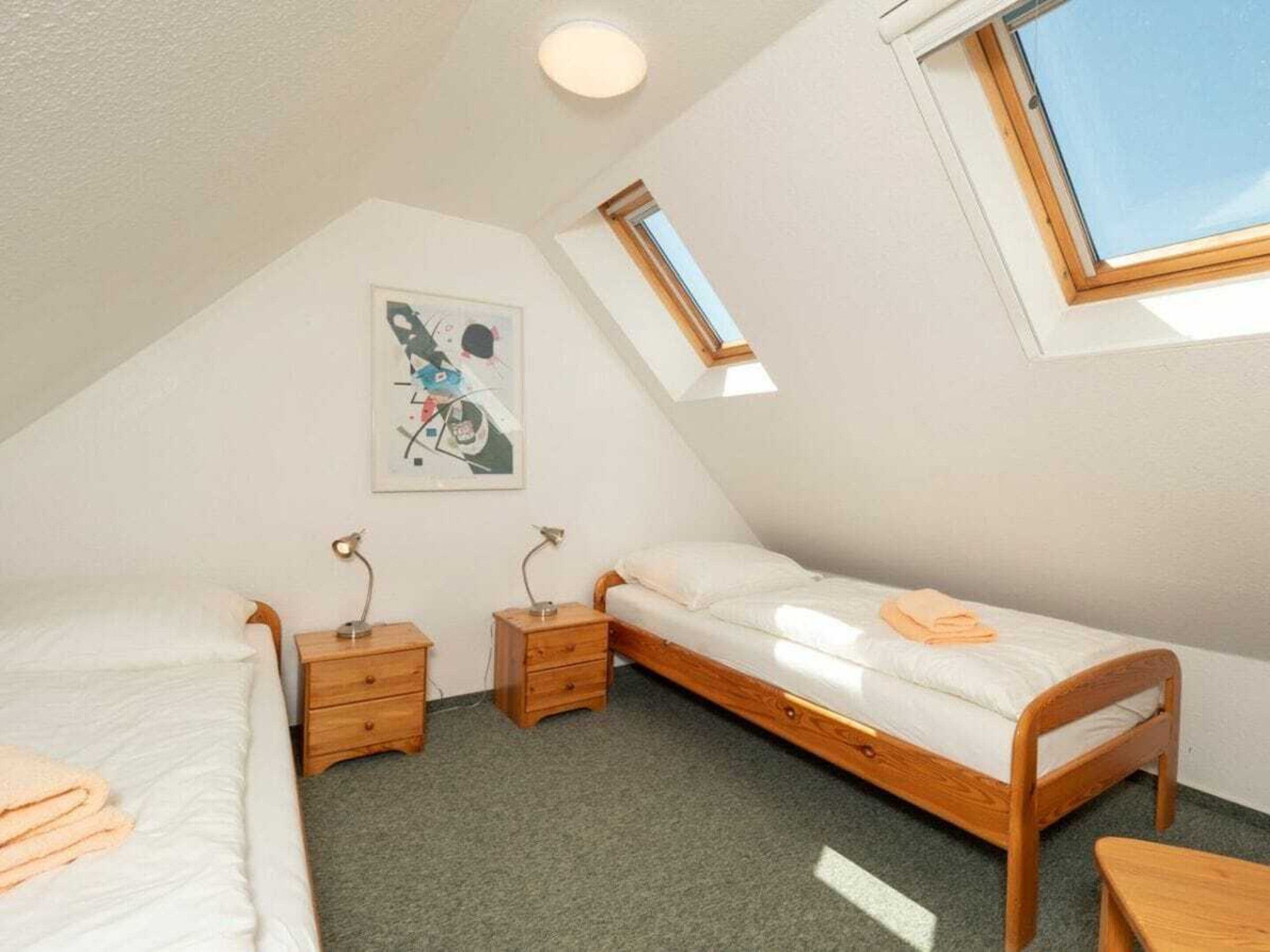 Un dormitorio ático pequeño y triangular con dos camas individuales, un escritorio de madera y un tragaluz.