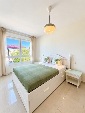 Ein Schlafzimmer mit einem Bett, Nachttischen, einem Fenster und einer Deckenleuchte.