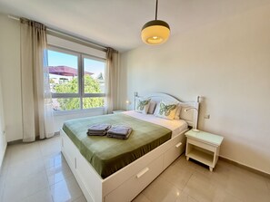 Ein Hotelzimmer mit Bett, Nachttisch, einem Fenster mit Vorhängen und Blick auf Grünfläche.