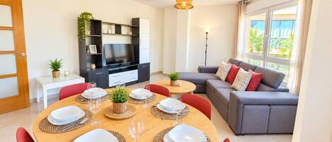 A modern living room with a dining area, a grey sofa, and a television.