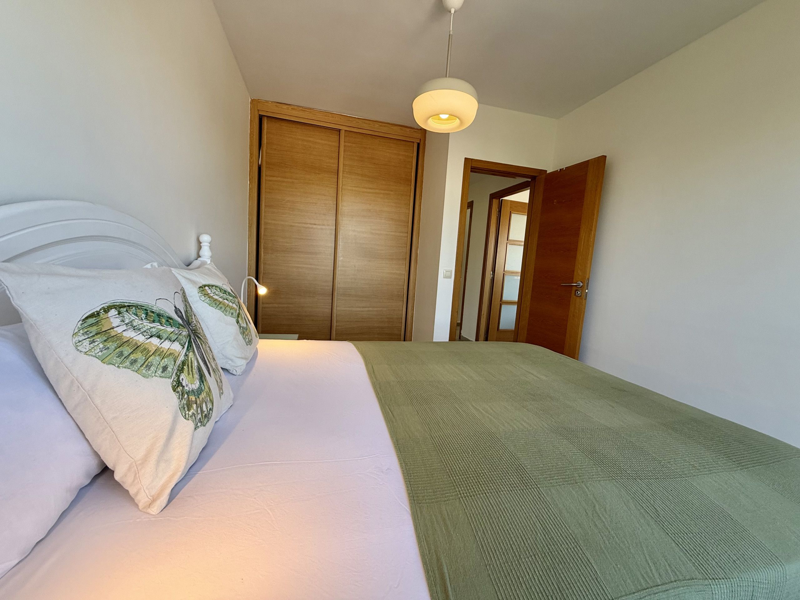 Un dormitorio con una cama, un almohadón con diseño de hoja, una lámpara colgante y un armario de madera.