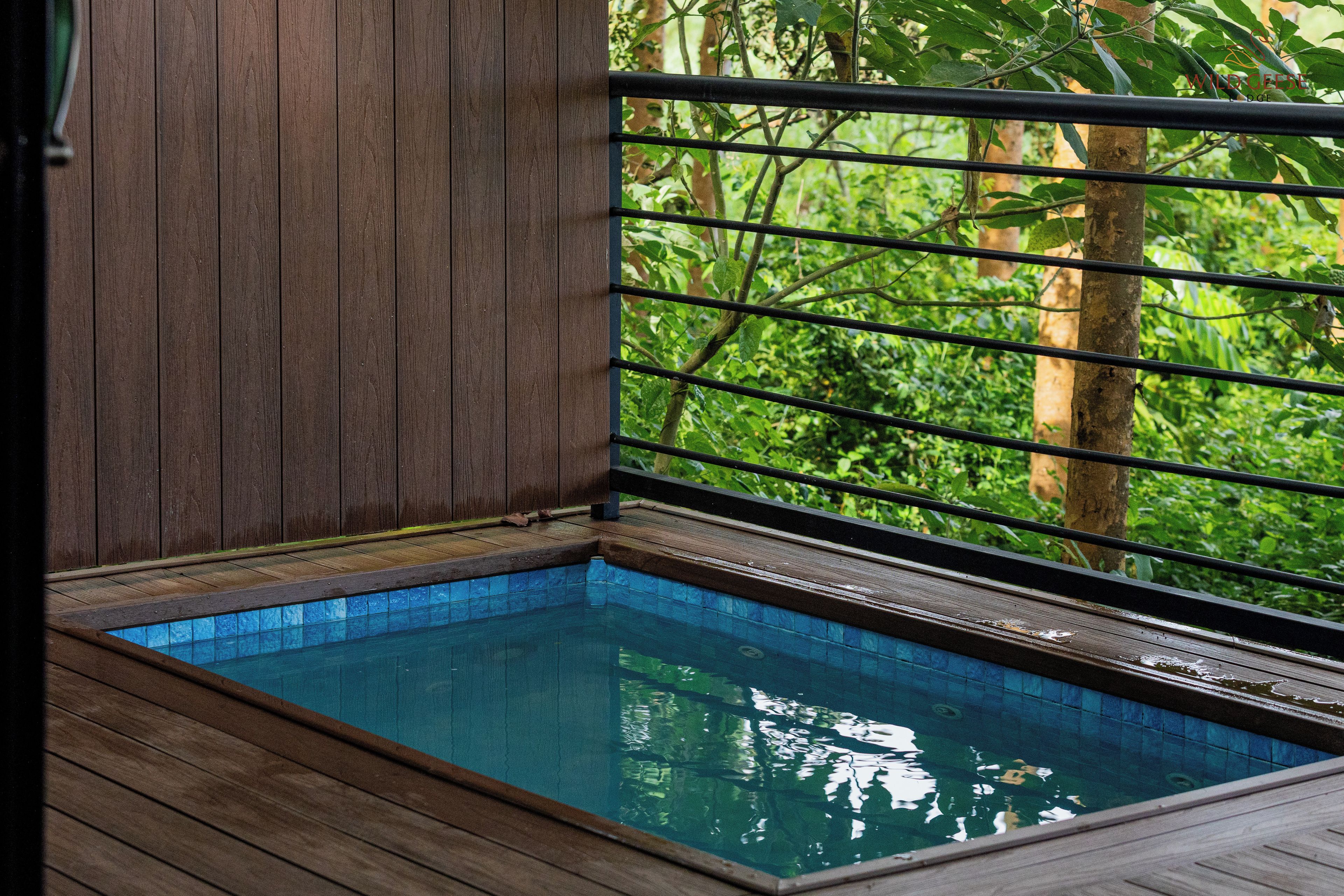 A wooden deck with a pool, surrounded by greenery.