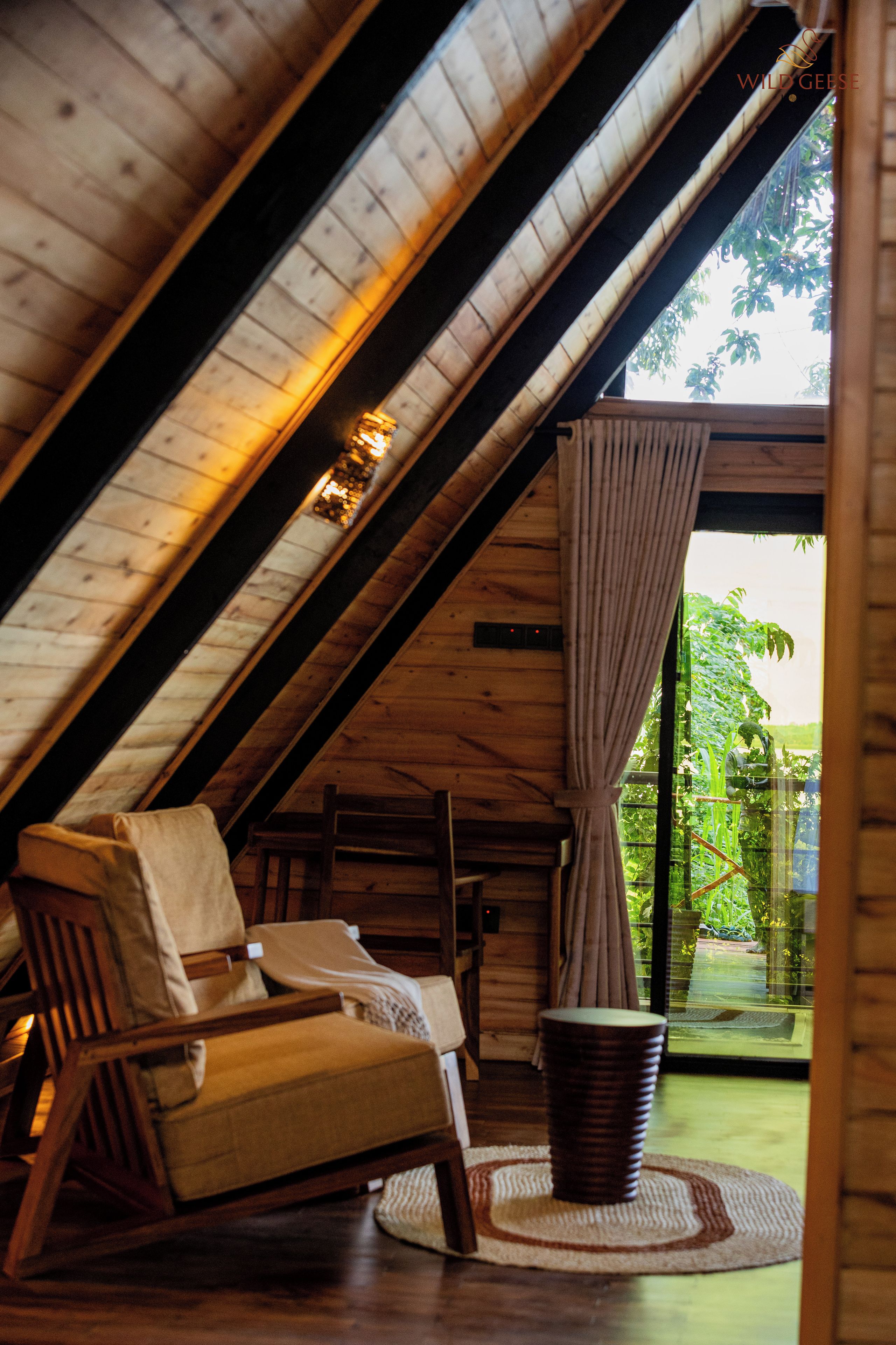A cozy room with a sloped ceiling, a wooden chair, a small table, and a view of greenery outside.