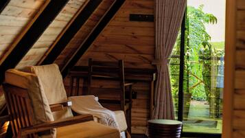 A cozy room with a sloped ceiling, a wooden chair, a small table, and a view of greenery outside.