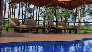 A poolside area with lounge chairs and umbrellas, surrounded by trees.