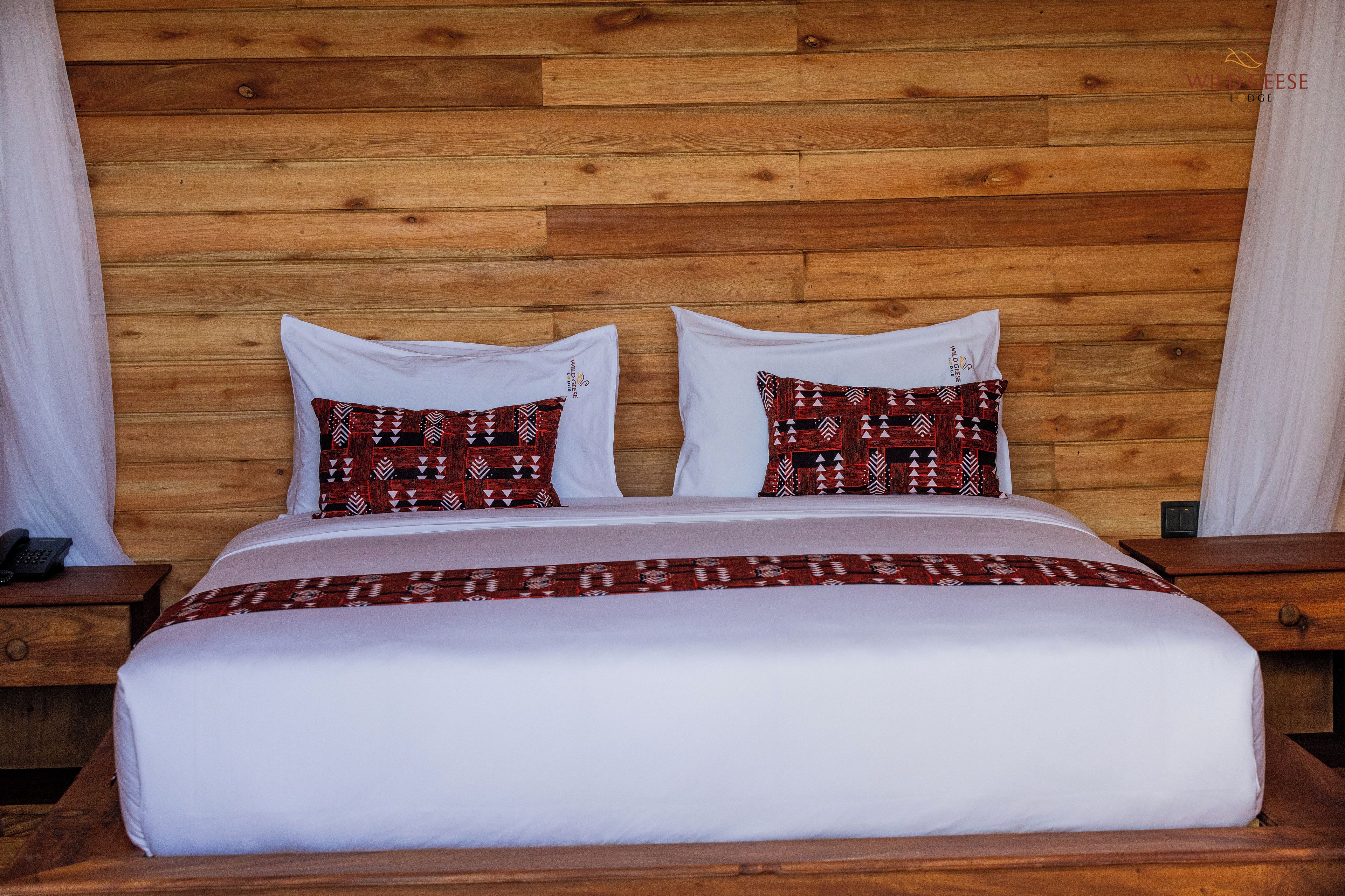 A bed with a white bedspread and two patterned pillows, set against a wooden headboard.