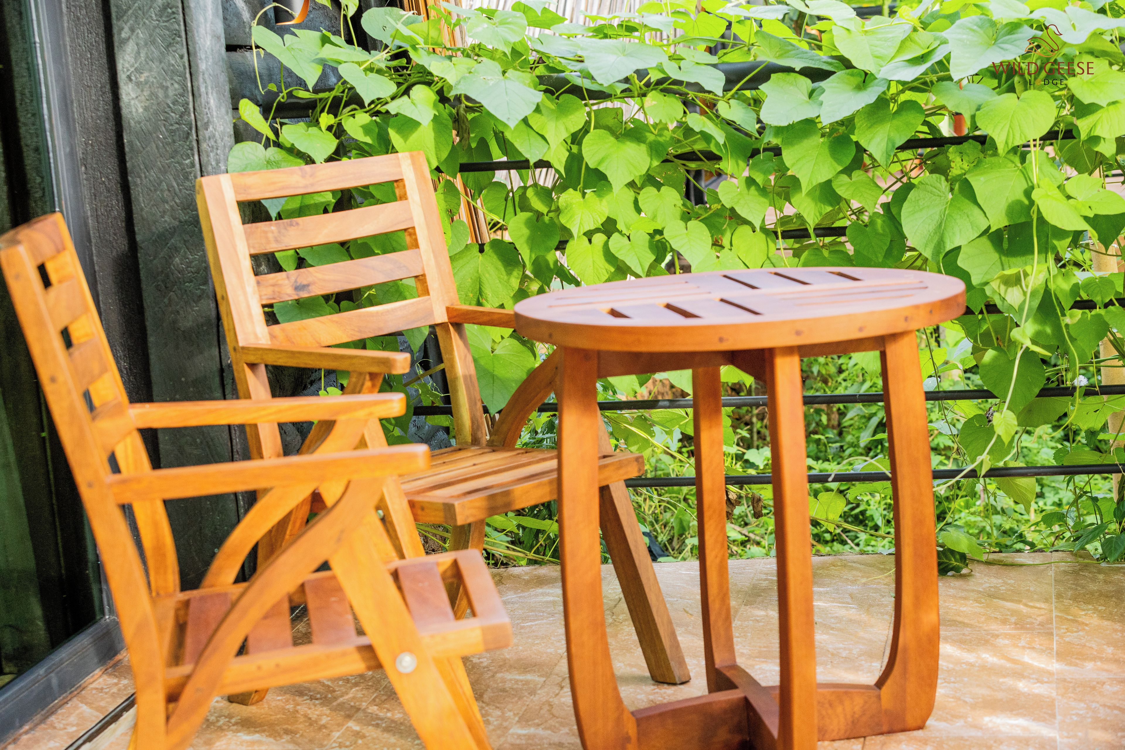 A wooden chair and table set on a tiled floor, with a green leafy background.