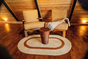 Una habitación acogedora con pisos y paredes de madera, que incluye dos sillones con cojines y una pequeña mesa de madera con un tapete tejido.
