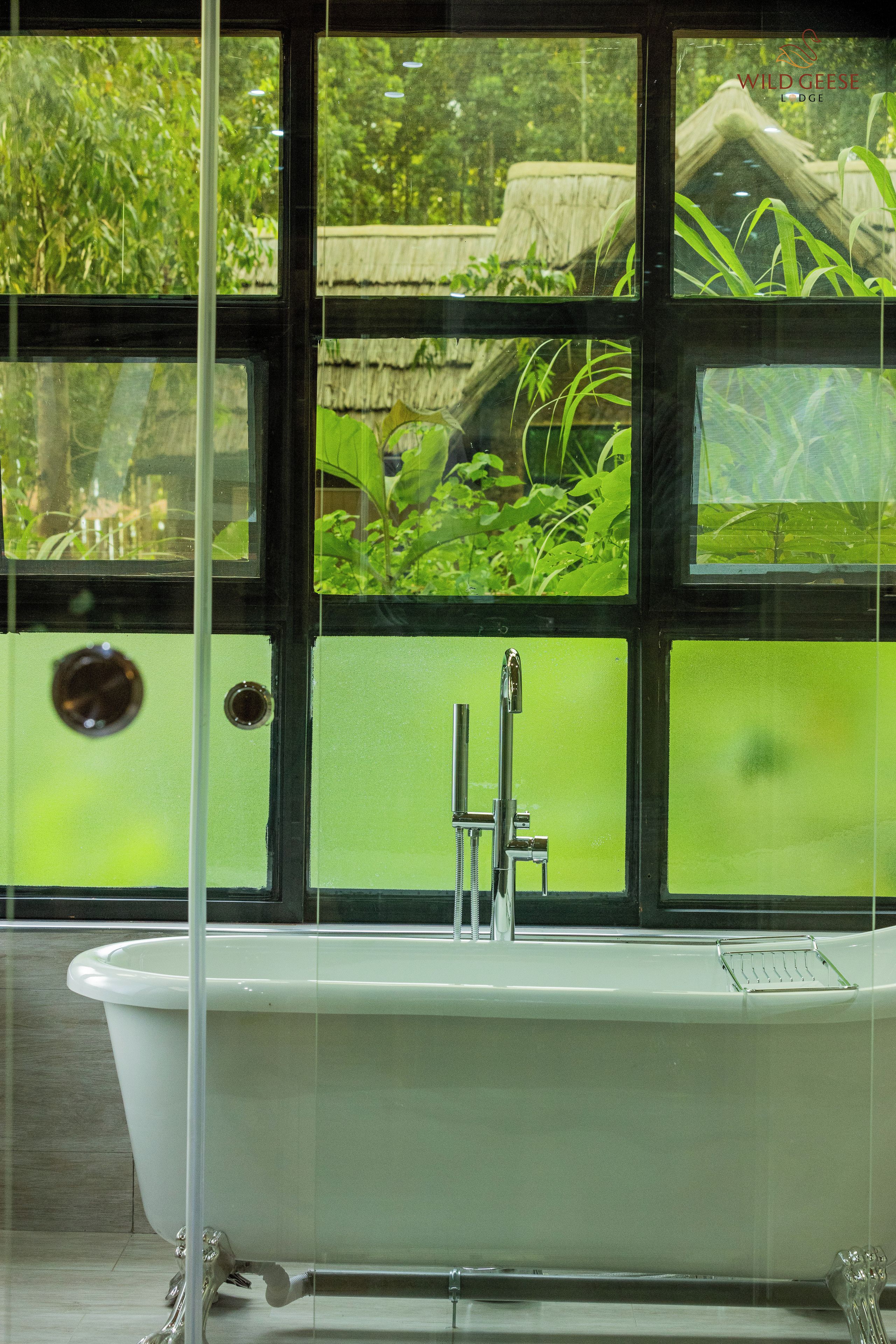 Un baño con bañera, una ventana con vistas a zonas verdes y una zona de ducha.