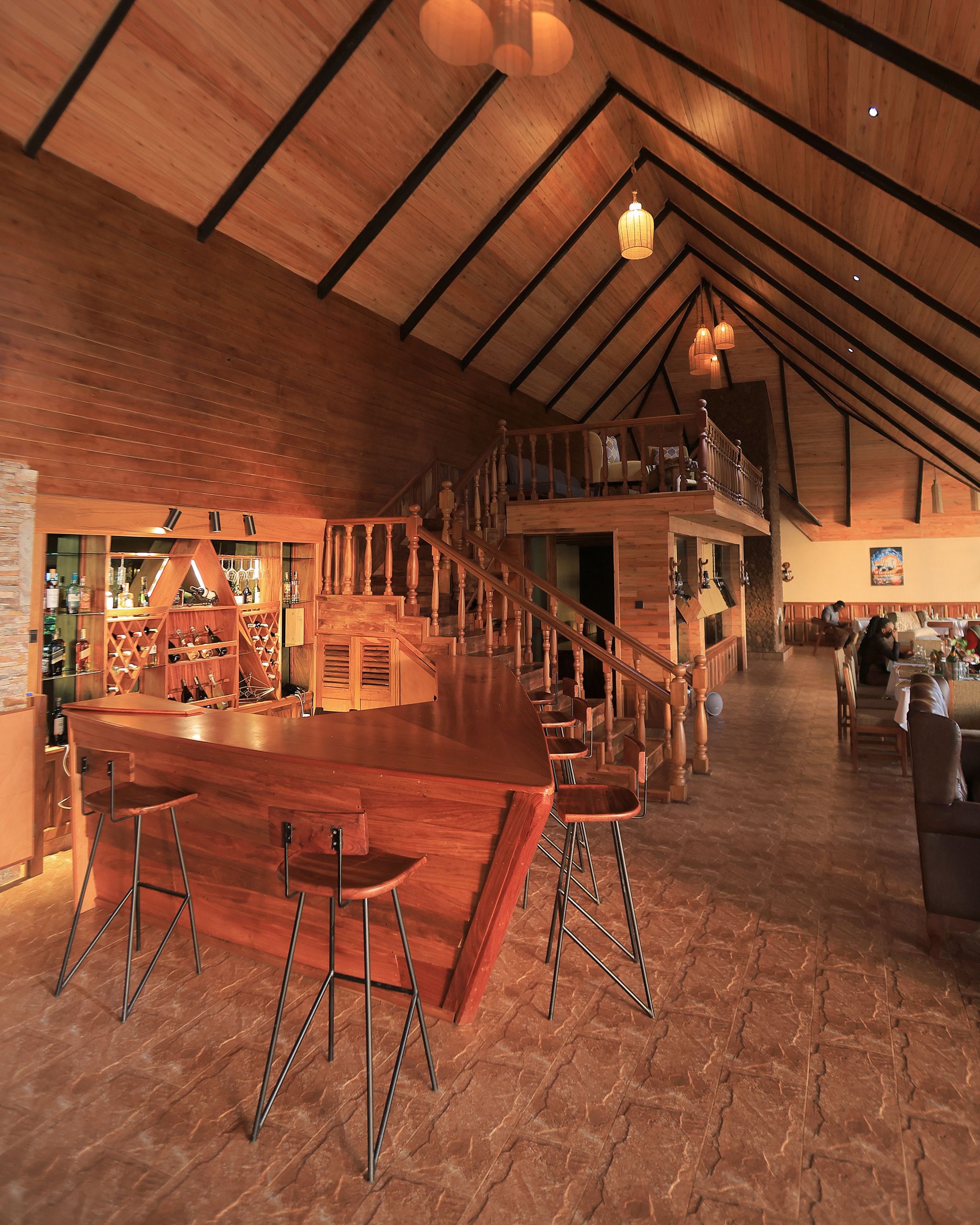 Uma área de bar espaçosa com pé direito alto e vigas de madeira, incluindo disposição de banquetas e um espaço para adega.