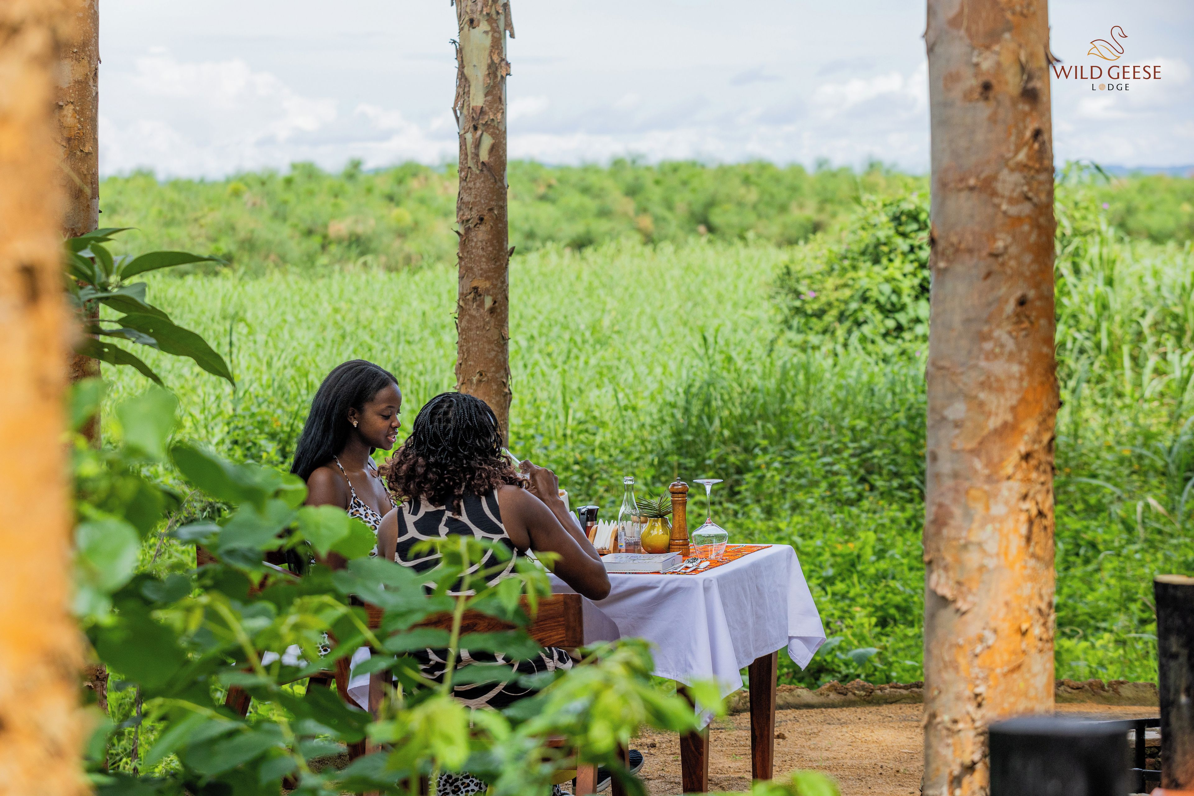Two people dining at an outdoor table with a view of a green field.