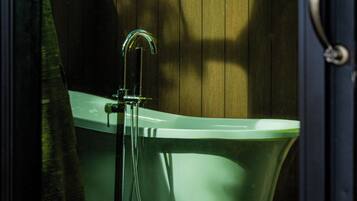 A bathtub with a shower head, positioned against a wooden wall with trees visible through the window.